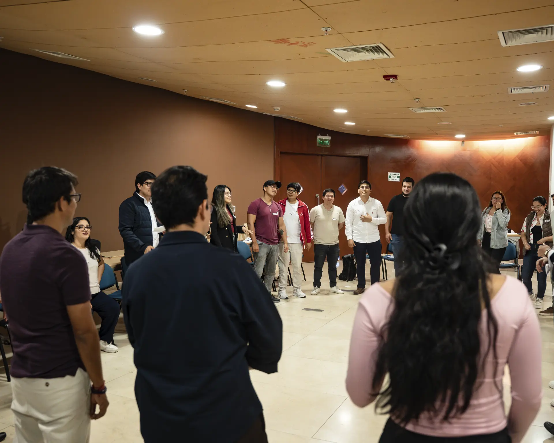 Círculo de participantes de pie durante un ejercicio presencial de RECOProgramando en Lima