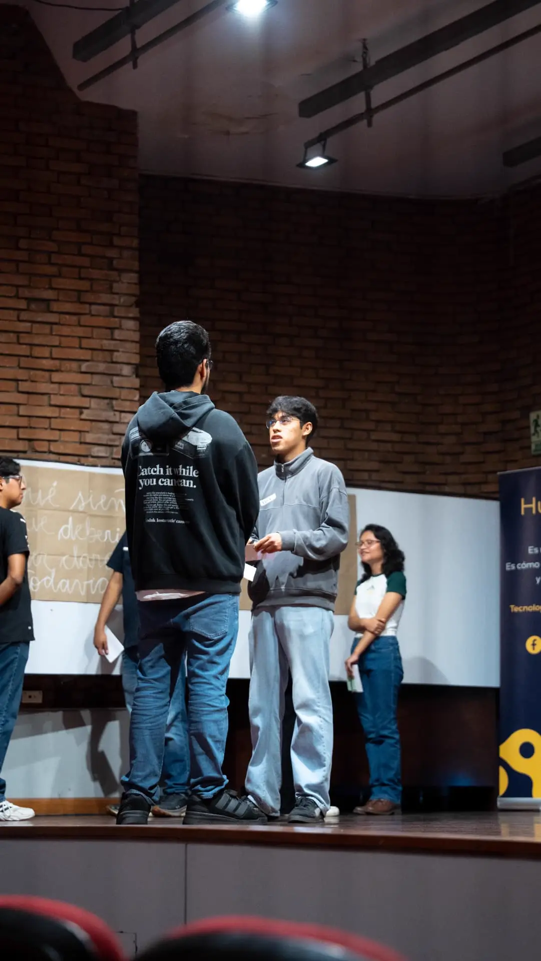 Dos estudiantes conversando de pie sobre el escenario