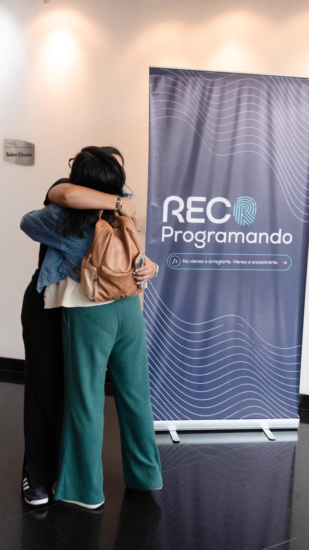 Dos participantes abrazándose junto al banner de RECOProgramando al cierre