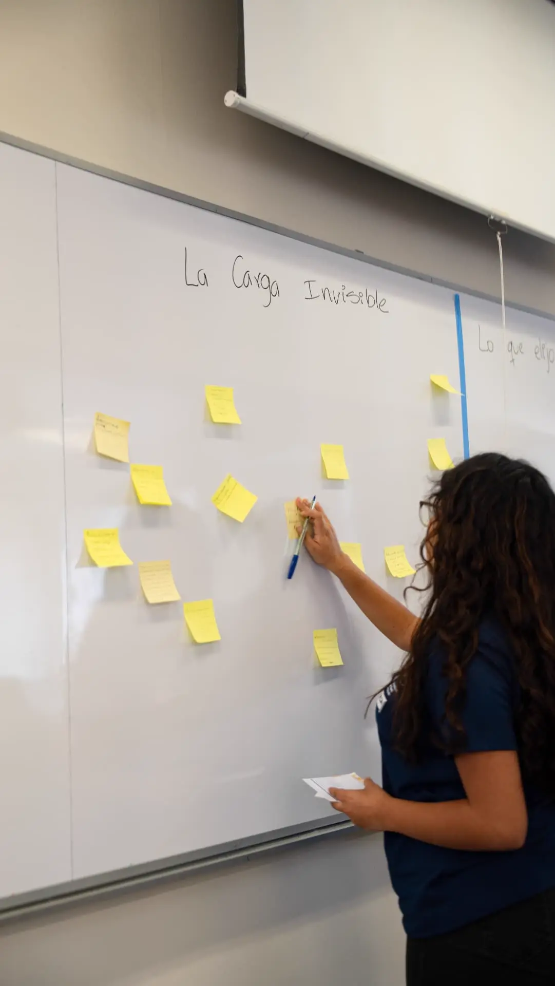 Estudiante pegando un post-it bajo el título «La carga invisible» en la pizarra