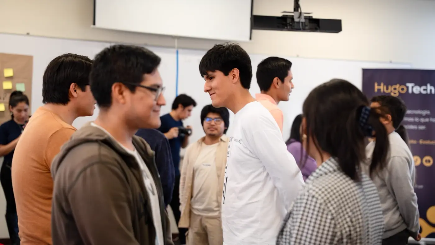 Estudiantes conversando de pie en parejas dentro del aula