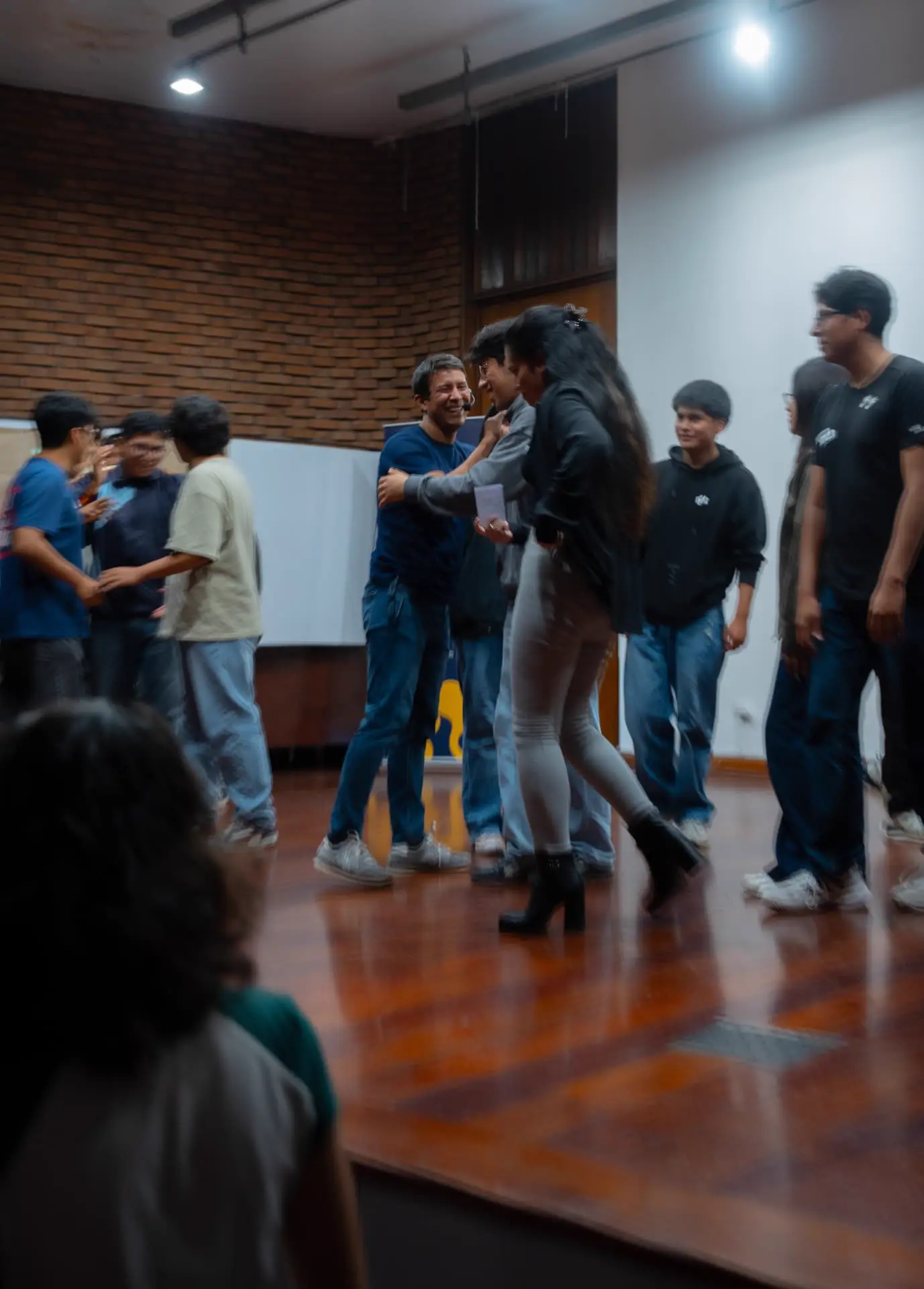 Estudiantes intercambiando tarjetas y abrazos sobre el escenario