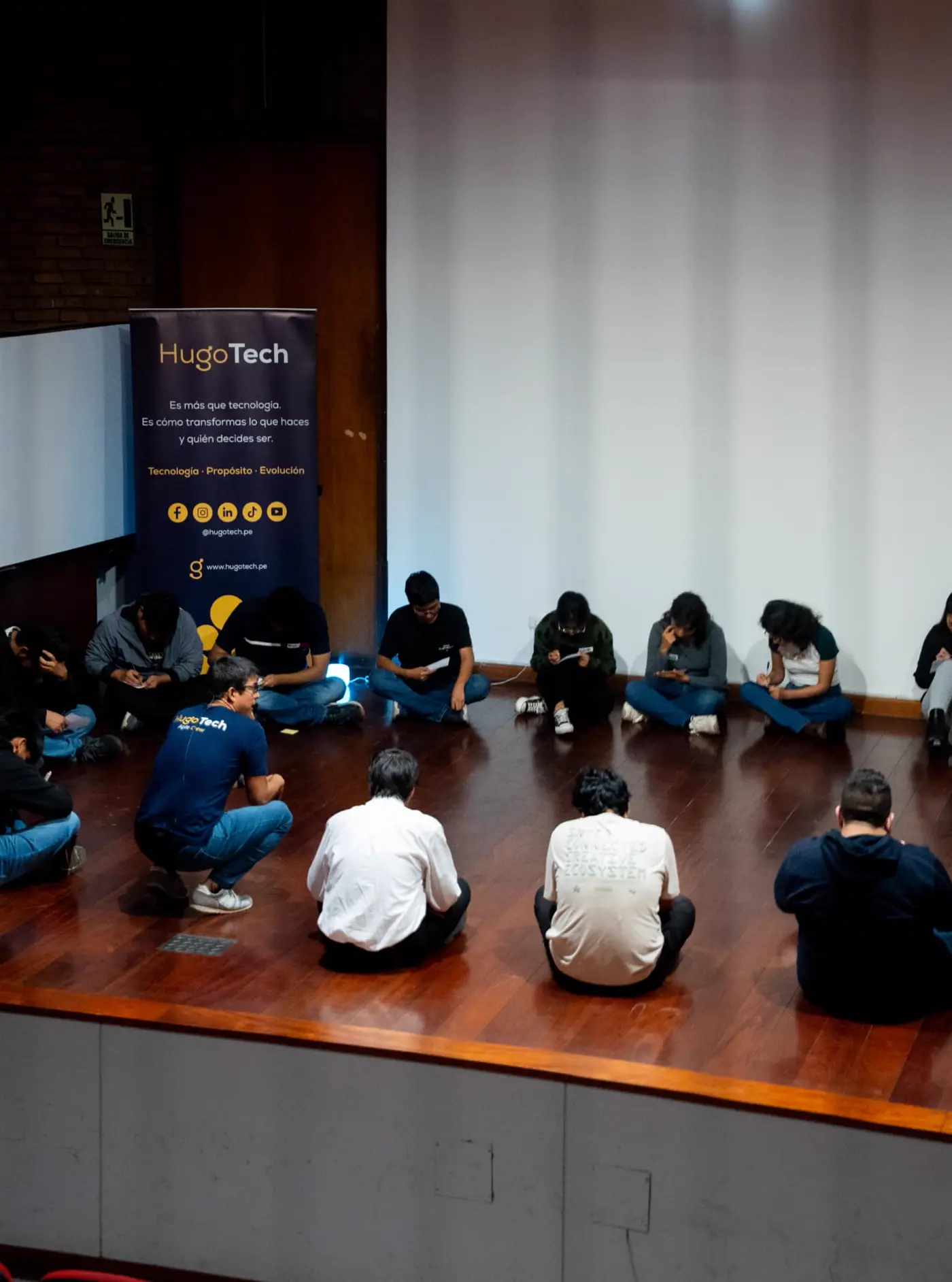 Círculo de estudiantes sentados en el piso escribiendo con Hugo facilitando