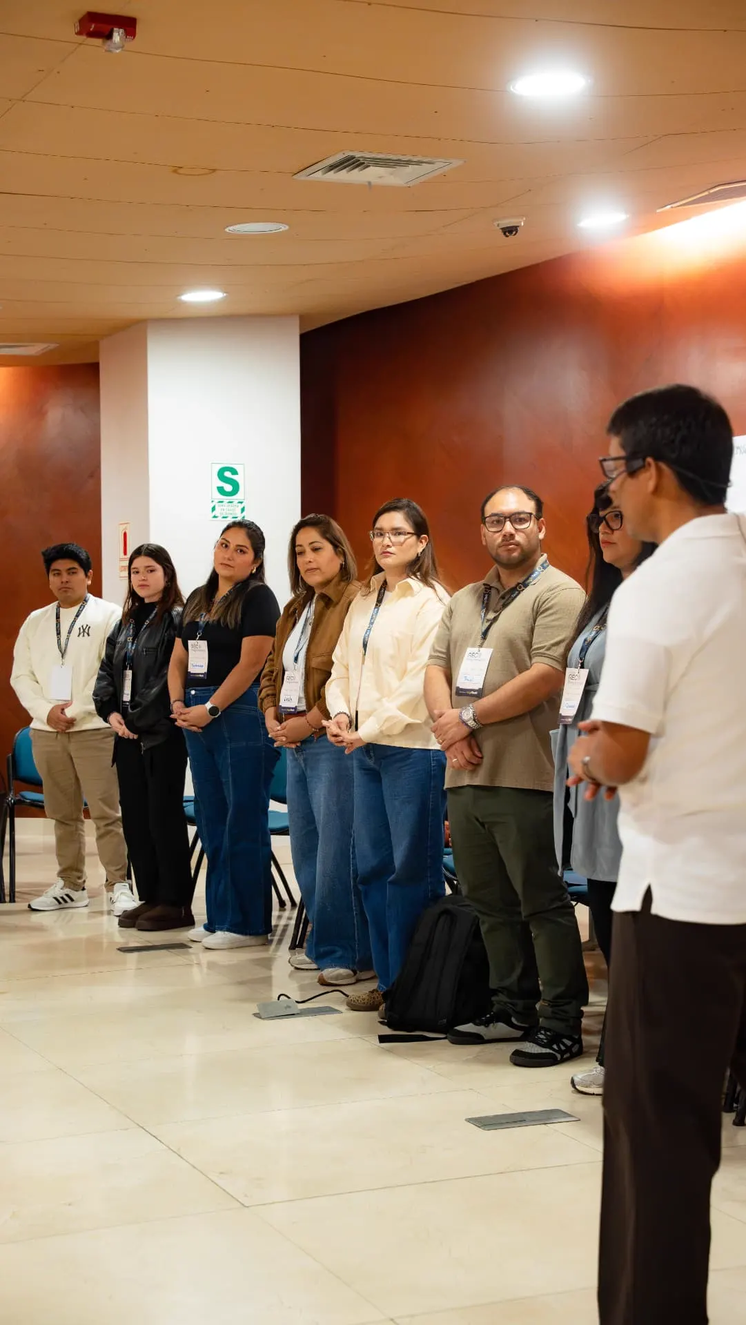 Grupo de participantes de pie escuchando en silencio al facilitador